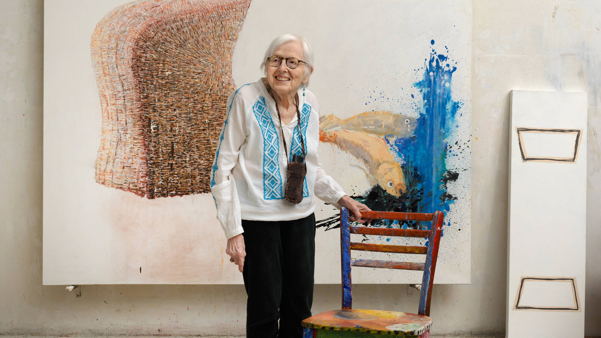 Photographic portrait of artist Vera Klement in front of one of her paintings.